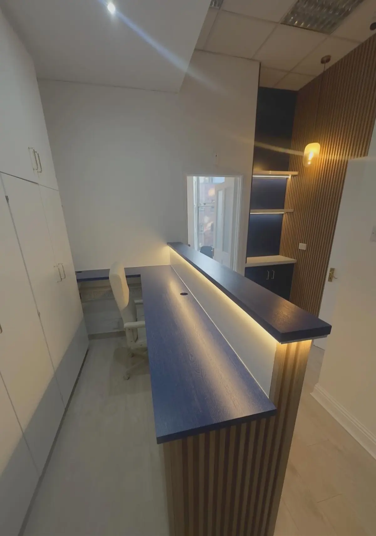 Reception with illuminated desk, storage wall and slatted panelling